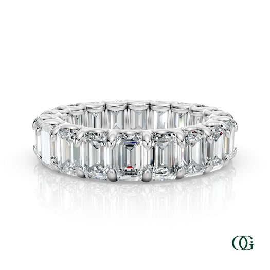 W | A White gold eternity ring featuring a continuous row of emerald-cut clear diamonds, set against a clean white background with a soft reflection below.