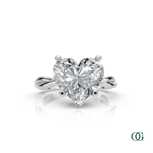 W | A heart-shaped diamond engagement ring in a white gold setting with a twisted band, shown on a clean white background with a soft reflection.