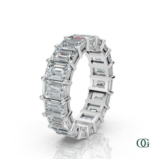 W | A white gold eternity ring featuring a row of emerald-cut clear diamonds, set against a clean white background with a soft reflection.