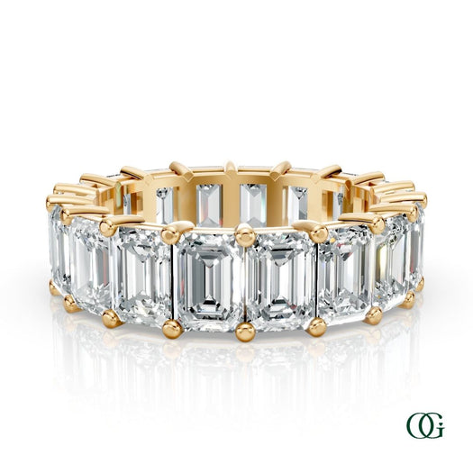Y | A yellow gold eternity ring featuring a row of emerald-cut clear diamonds, set against a clean white background with a soft reflection.