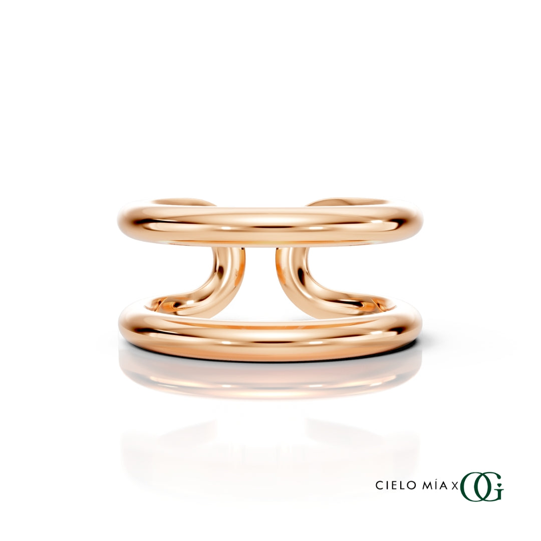 R | A polished rose gold double-band ring with a sculptural, intertwined curved design, displayed on a clean white background with a soft reflection and the brand logo 'CIELO MIA x OG' in the bottom right corner.