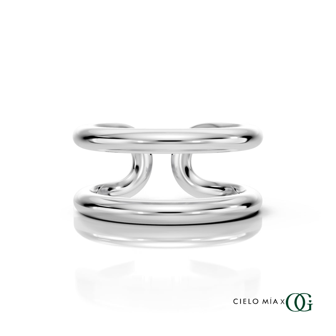 W | A polished white gold double-band ring with a sculptural, intertwined curved design, displayed on a clean white background with a soft reflection and the brand logo 'CIELO MIA x OG' in the bottom right corner.