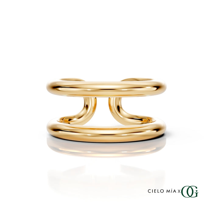 Y| A polished gold double-band ring with a sculptural, intertwined curved design, displayed on a clean white background with a soft reflection and the brand logo 'CIELO MIA x OG' in the bottom right corner.