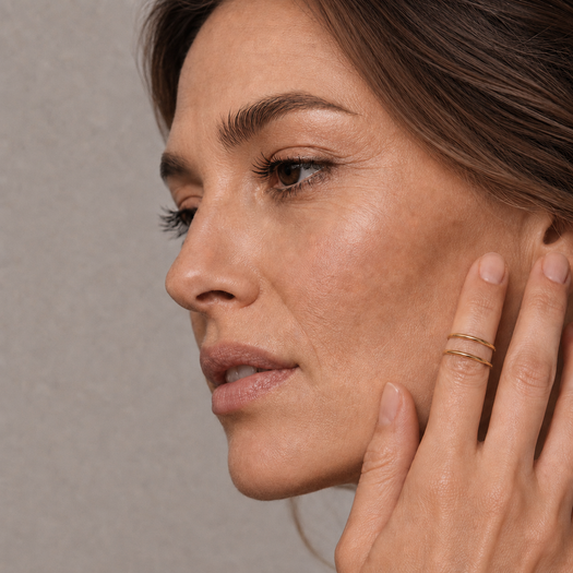 Y| A polished gold double-band ring with a sculptural, intertwined curved design, displayed on a clean white background with a soft reflection and the brand logo 'CIELO MIA x OG' in the bottom right corner.