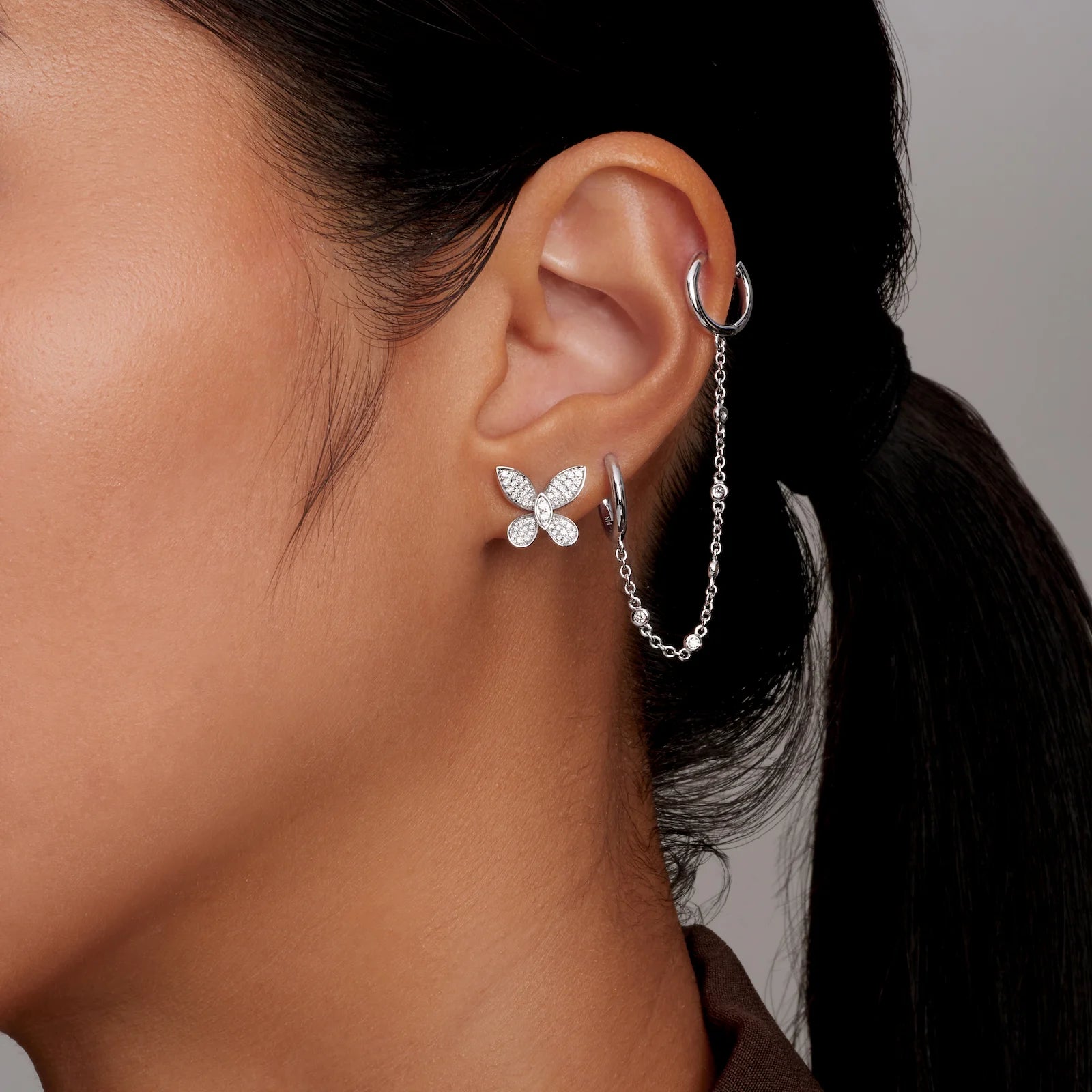 Close-up of a person wearing butterfly-shaped earrings with a neutral background
