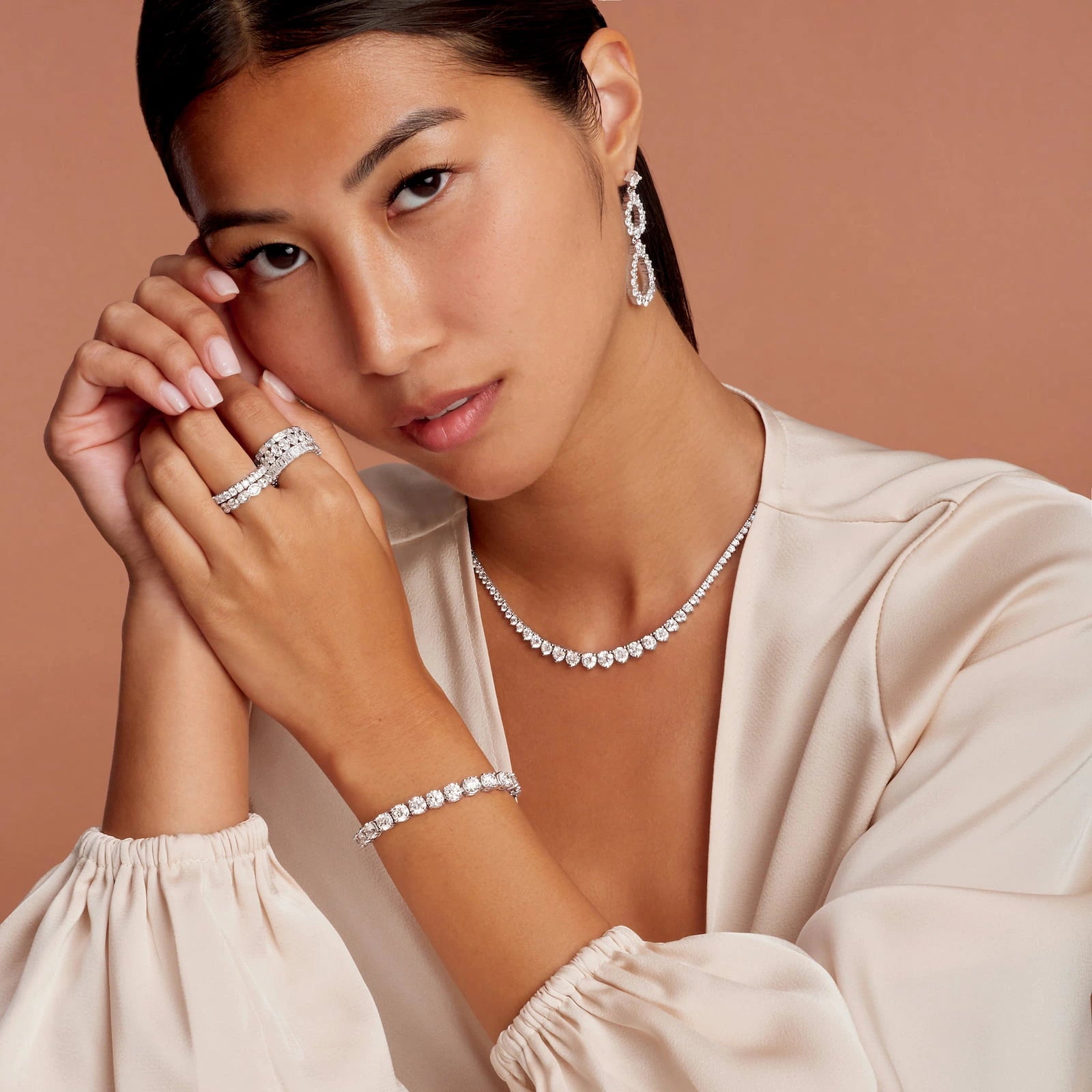 Woman wearing diamond jewelry including a necklace, bracelet, and ring on a beige background