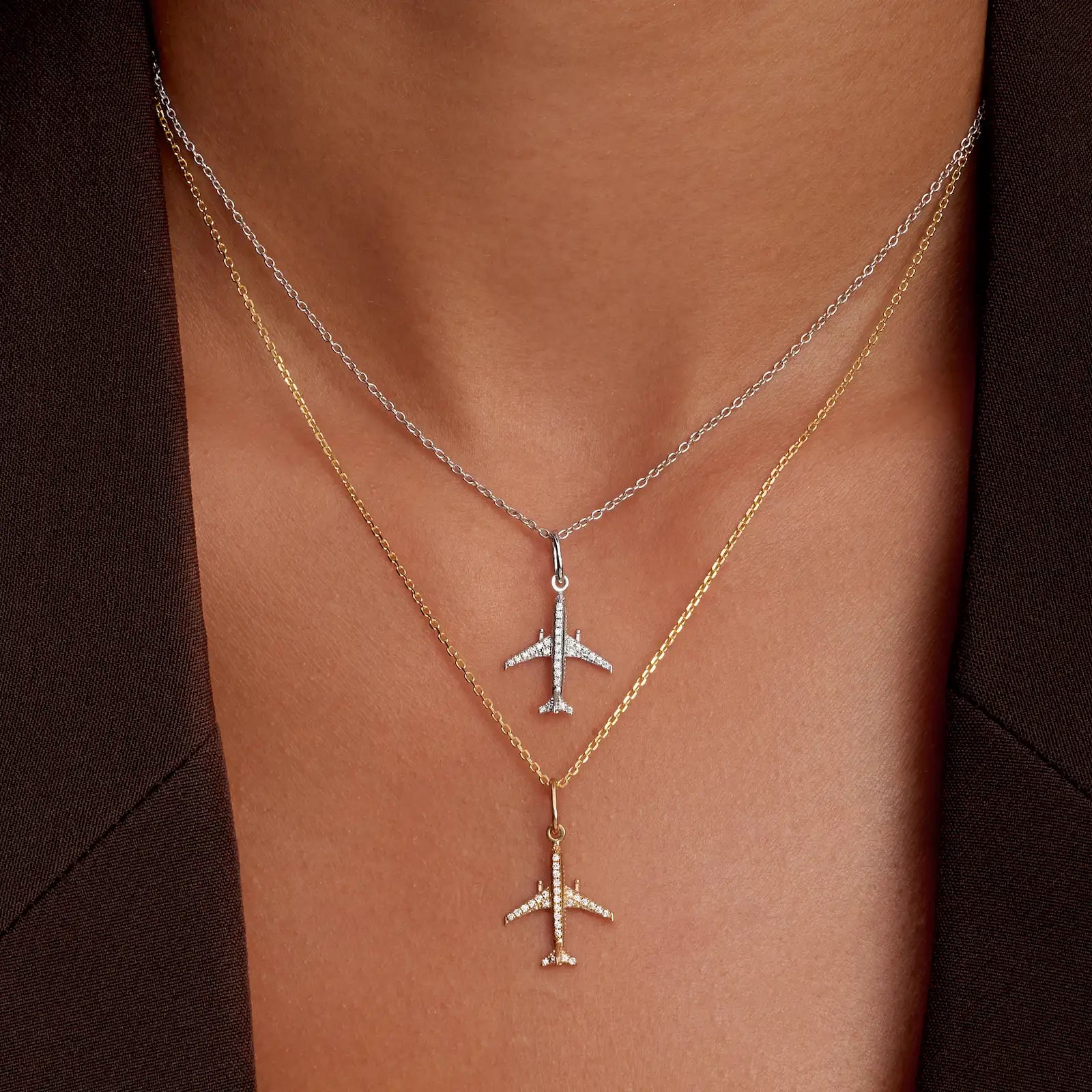 Two airplane-shaped pendants on necklaces against a neutral background